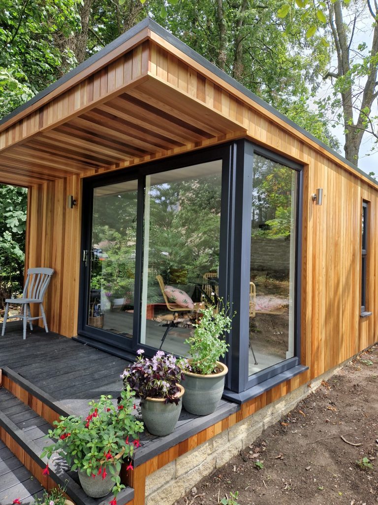 Timber-clad garden room with glass doors and planted containers outside