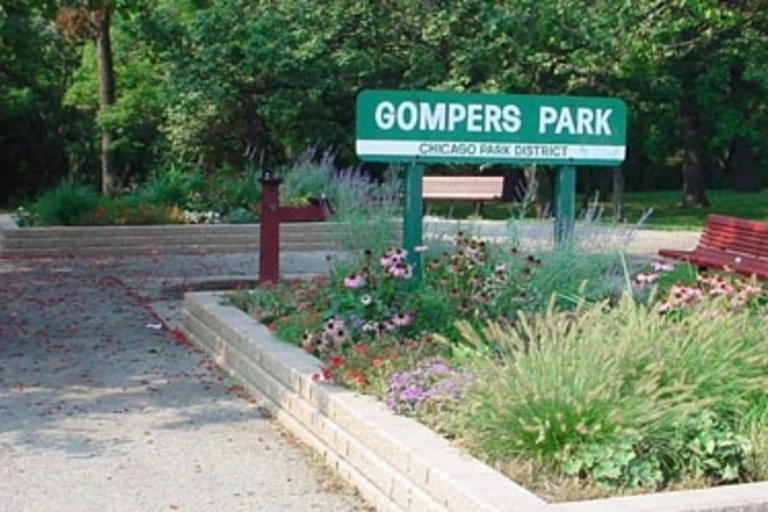 Señal de Gompers Park junto a un jardín y bancos.