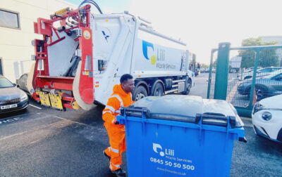 Lili Waste collection worker handling a blue bin beside a branded collection truck
