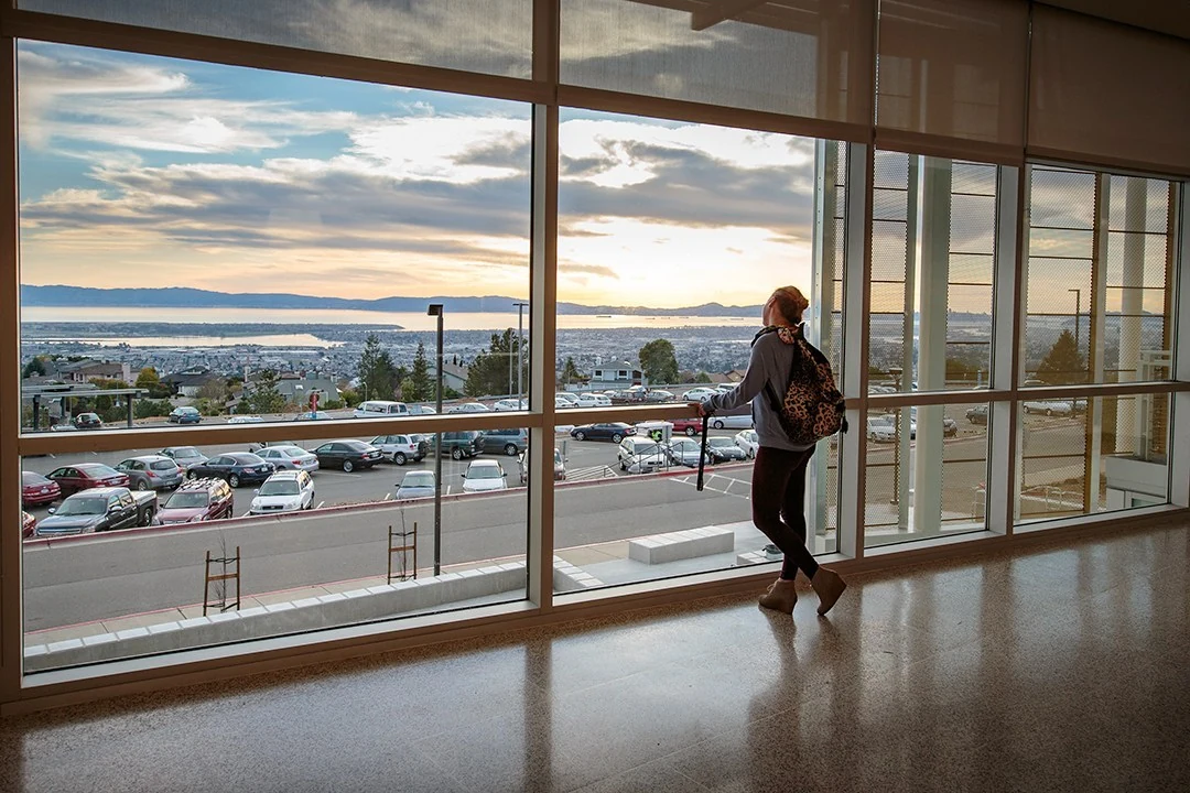 Una estudiante camina por el interior del campus de Merritt College, con ventanales hacia la bahía y Oakland