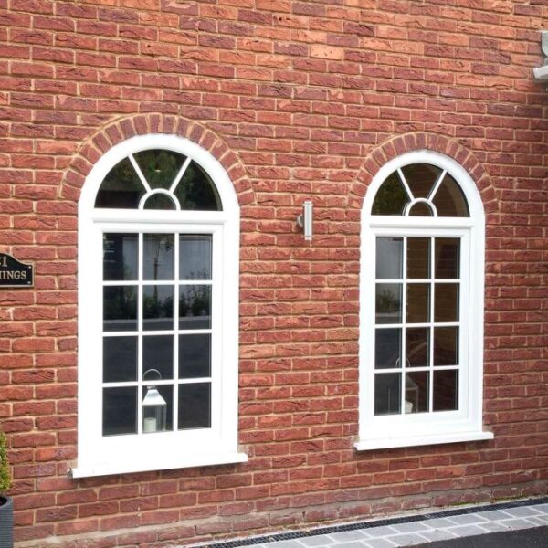 Two white arched windows with grid bars on a red brick wall.