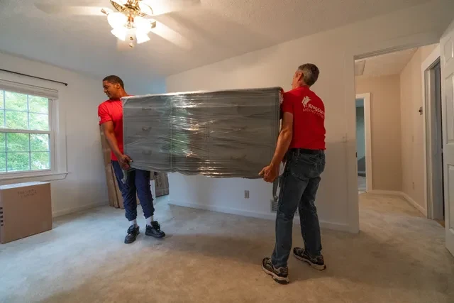 Dos trabajadores llevan un sofá envuelto dentro de una vivienda | Two movers carry a wrapped couch inside a home