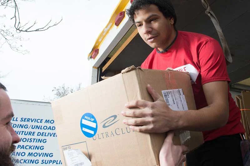 Trabajador de mudanzas con una caja junto a un camión | Moving worker carrying a box beside a truck