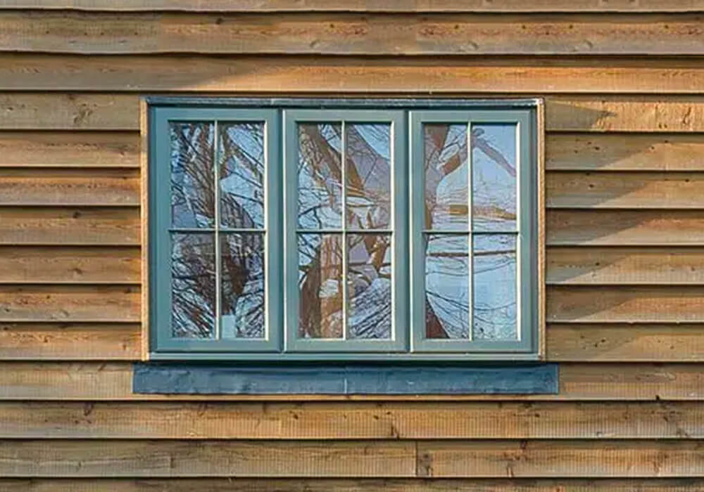 Ventanas correderas de madera en una fachada revestida de madera / Timber sliding windows in a timber-clad facade.