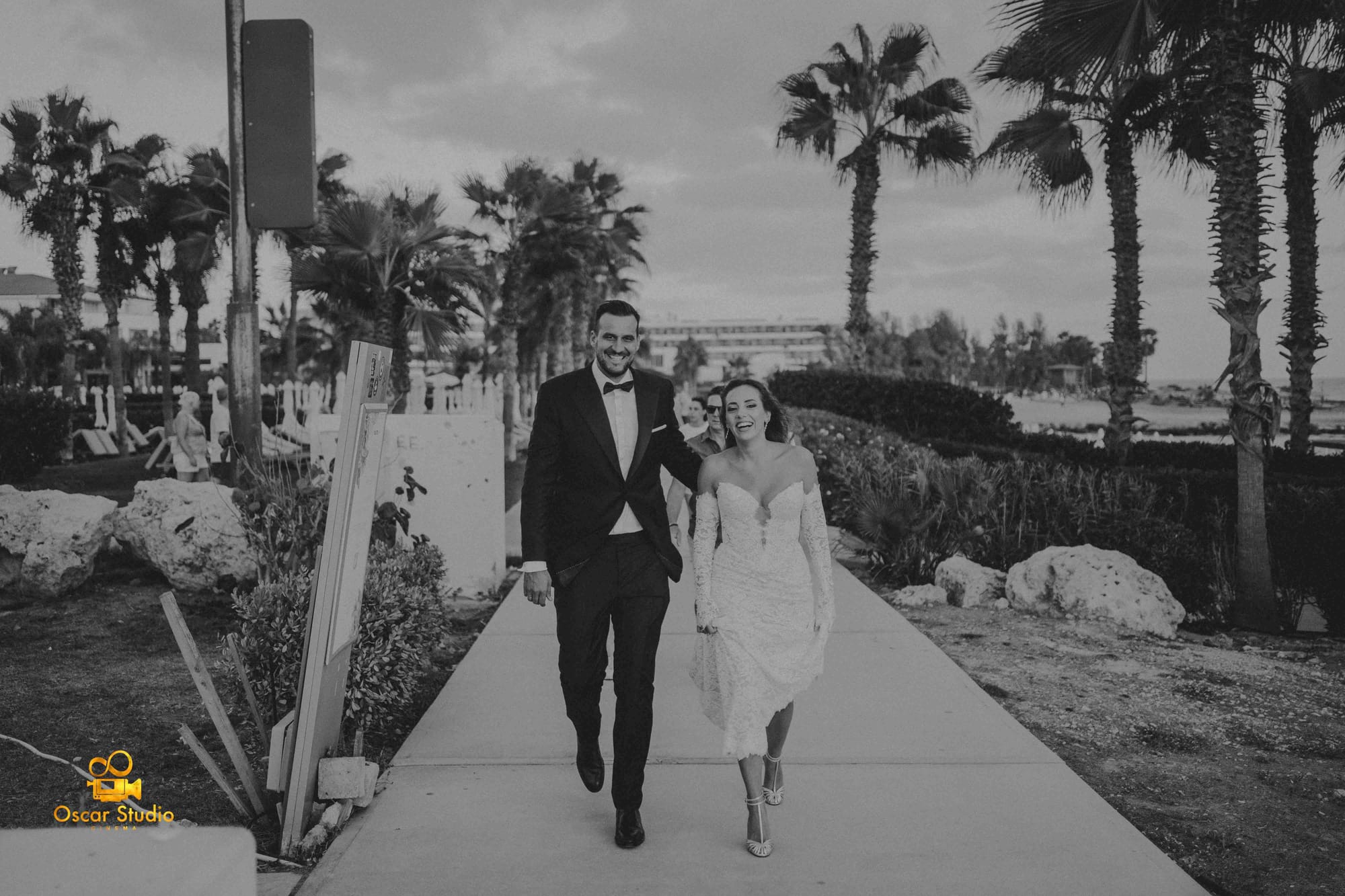 A wedding couple walking along a palm-lined path. / Pareja de novios caminando por un sendero flanqueado de palmeras.
