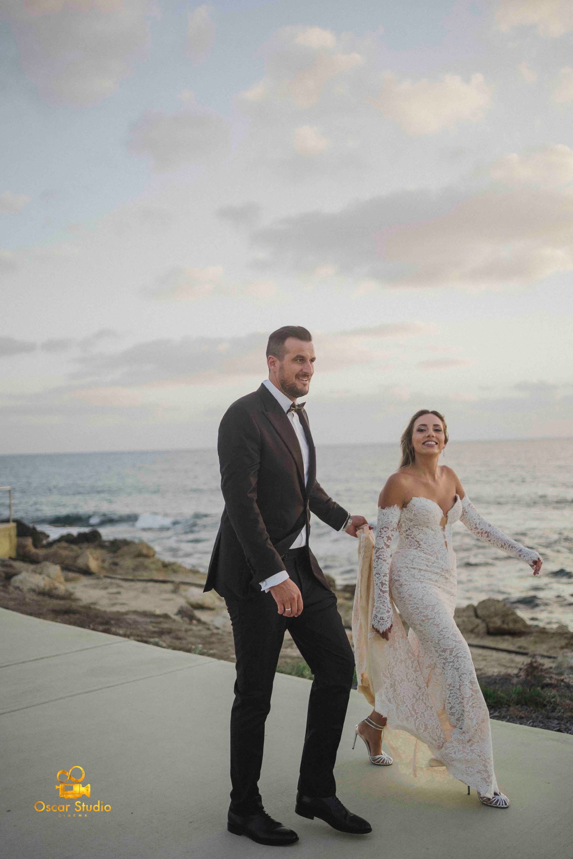 A newlywed couple walking beside the sea. / Pareja recién casada caminando junto al mar.