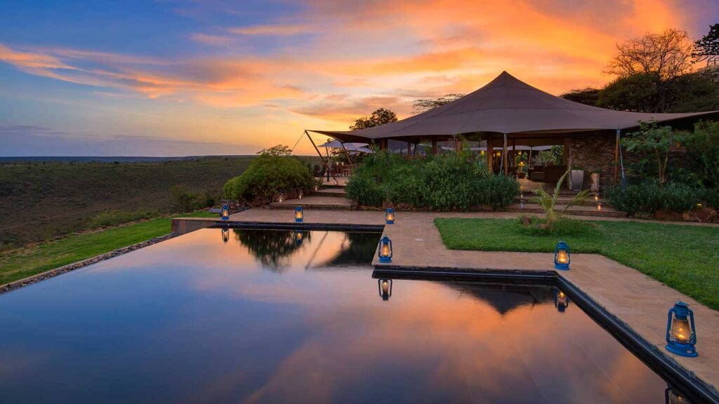A safari lodge pool and tented lounge at sunset.