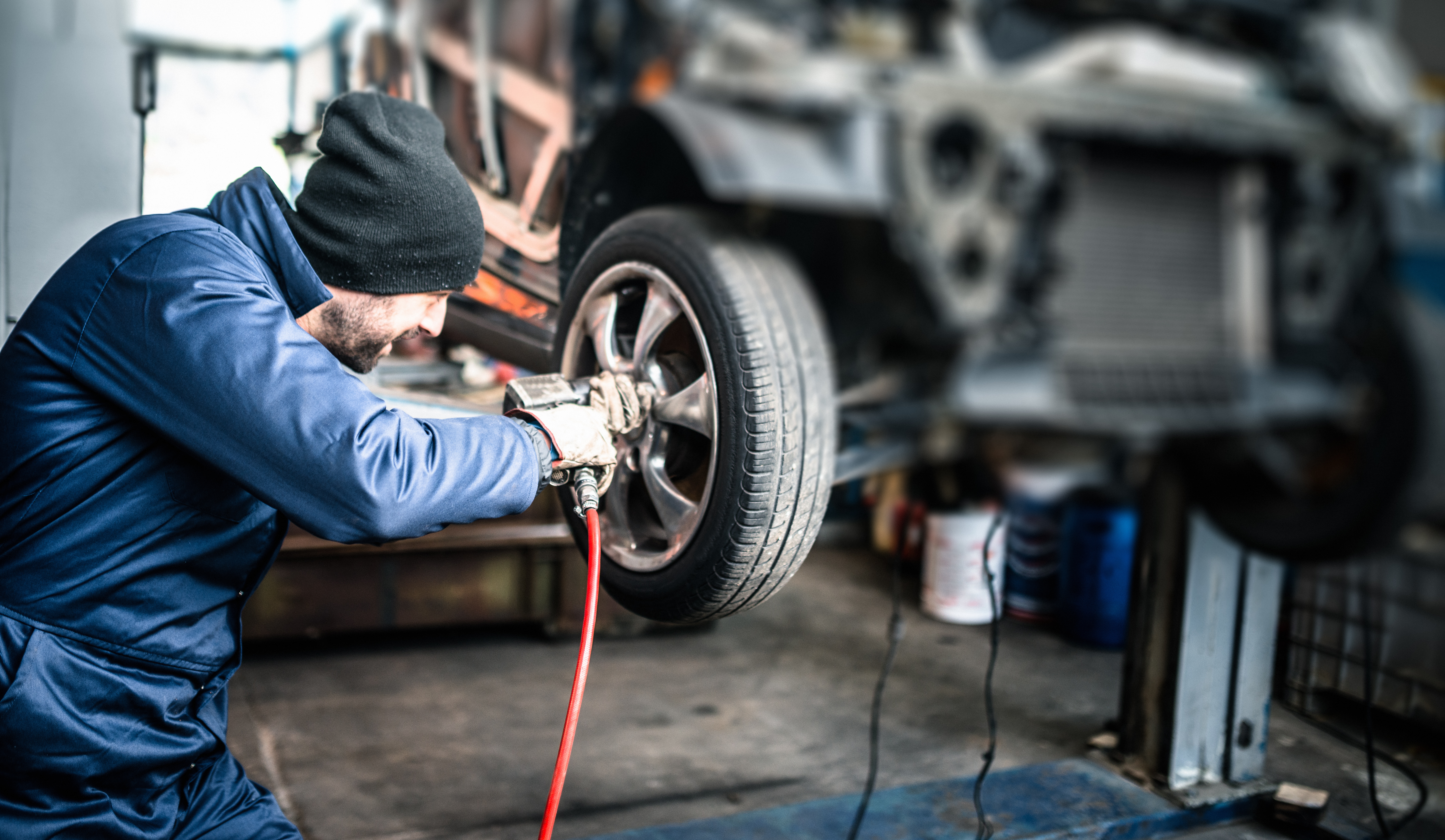 A technician uses an air hose while working on a vehicle tire in a service bay.