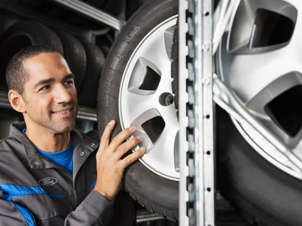 Mechanic inspecting a car wheel and tire in a service bay.