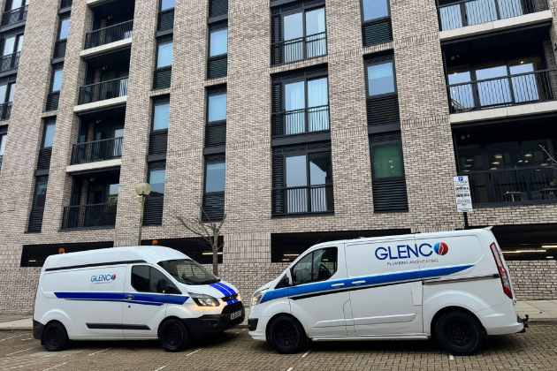 Two Glenco Plumbing & Heating service vans outside a city building.