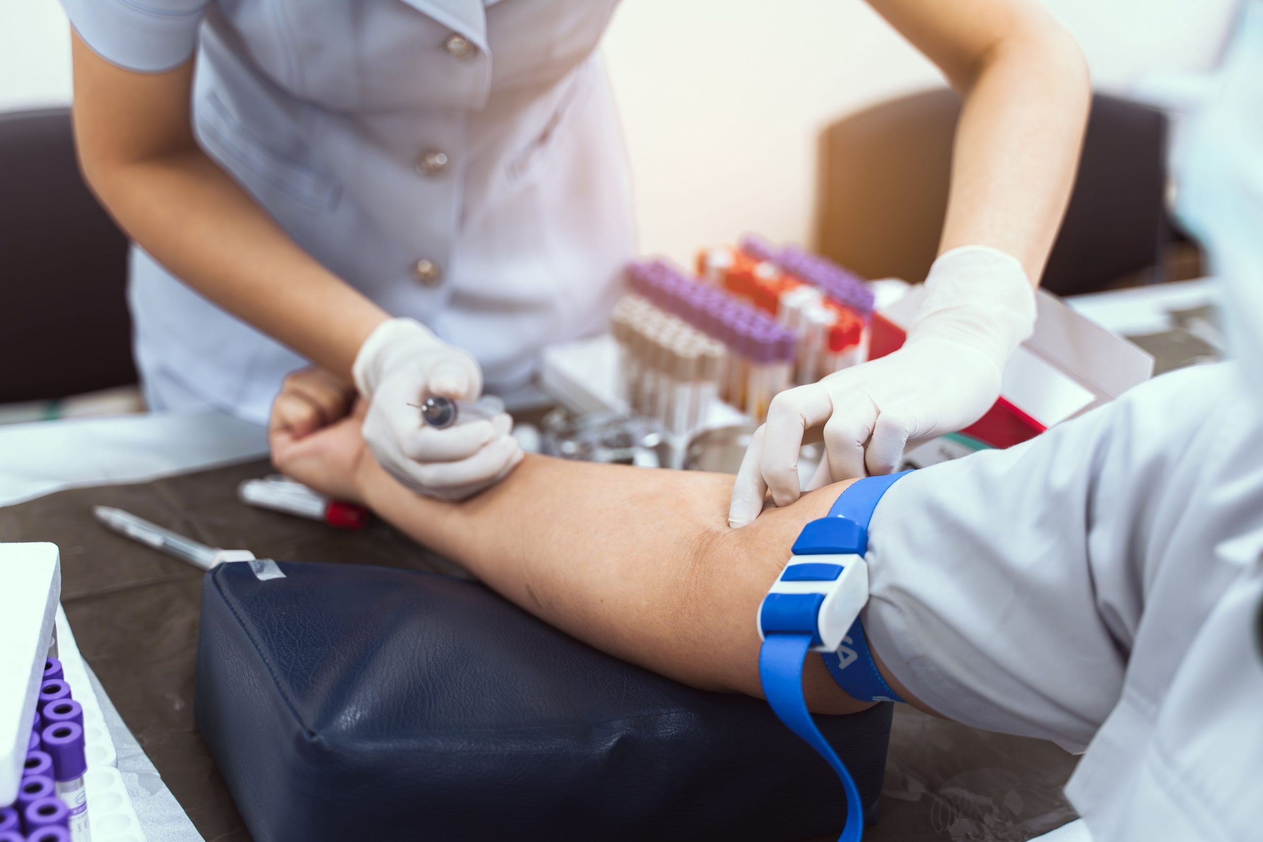 A clinician draws a blood sample from a seated patient.