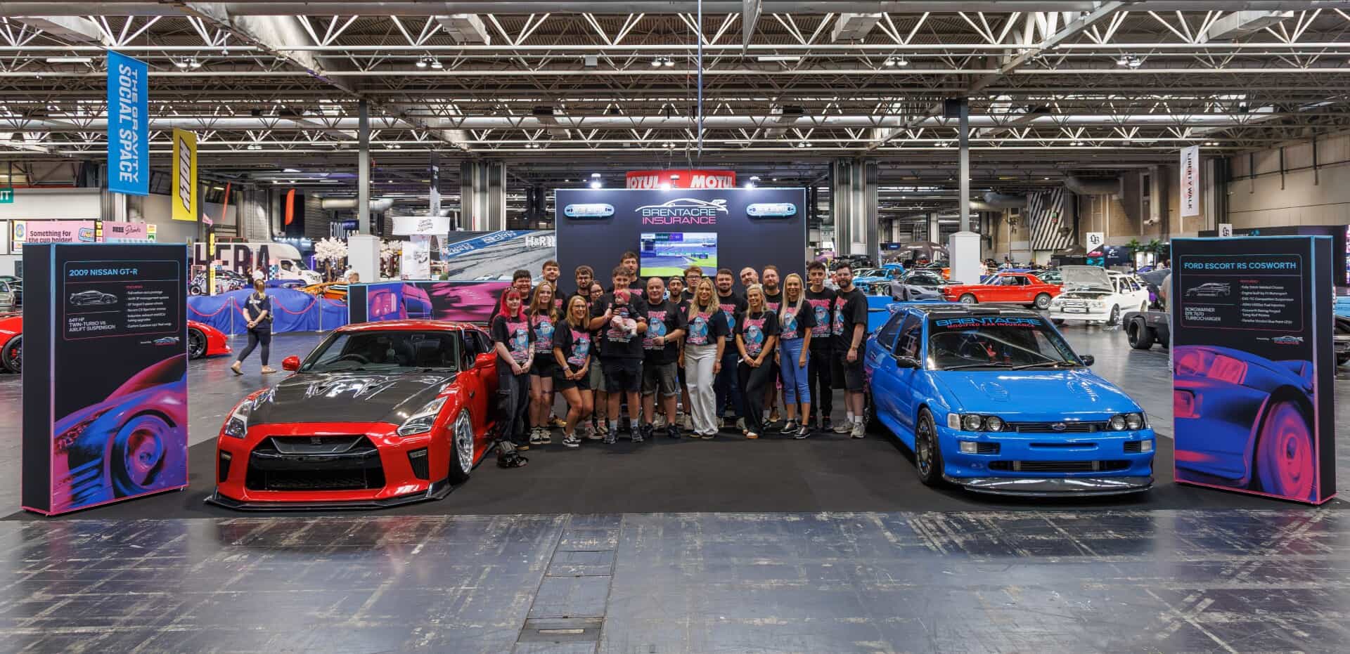 Puesto de Brentacre Insurance en un evento automovilístico, rodeado de coches modificados.