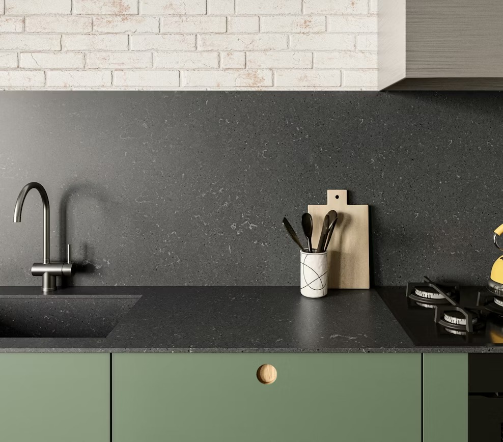 Encimera de superficie oscura instalada en una cocina con gabinetes verdes.