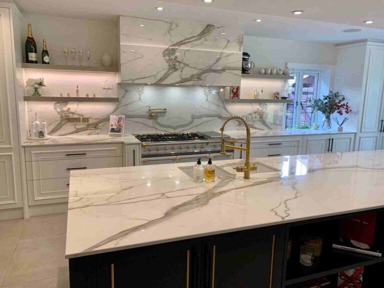 Cocina blanca con encimera e isla de piedra veteada y fregadero con grifo dorado.