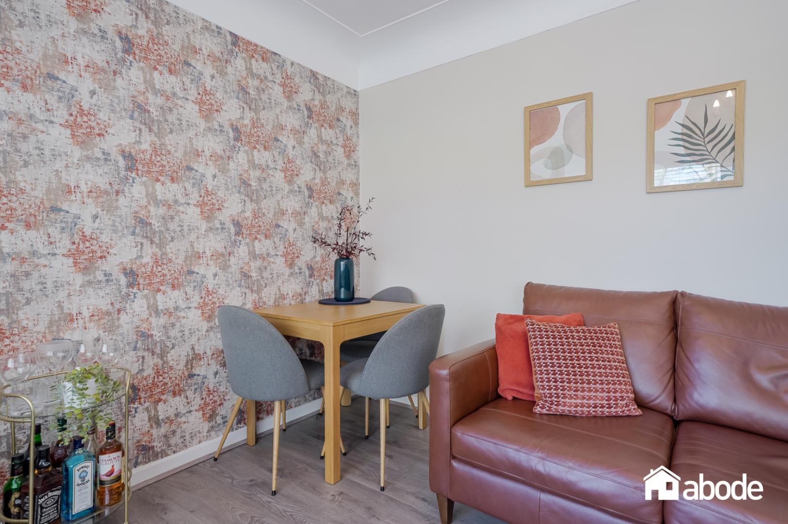 Sala amueblada con sofá, mesa de comedor y papel tapiz decorativo en una propiedad presentada por Abode.