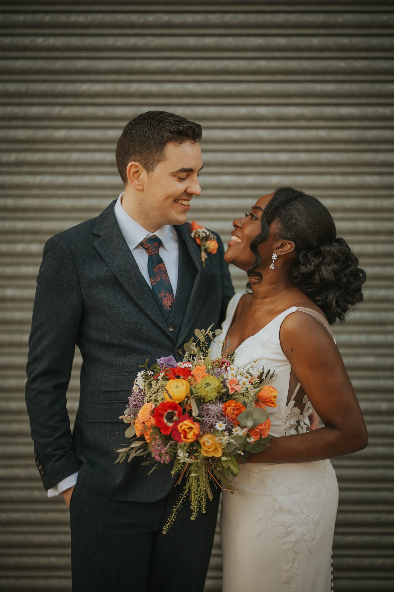 Pareja de recién casados junto a una composición floral de boda. / Newlyweds beside a wedding floral arrangement.