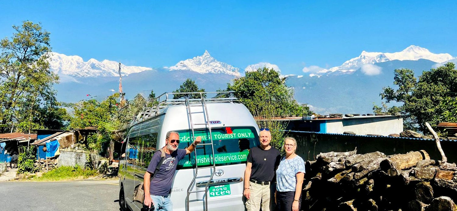 Furgoneta y varias personas junto a una carretera con montañas nevadas al fondo / A van and several people beside a road with snow-capped mountains in the background