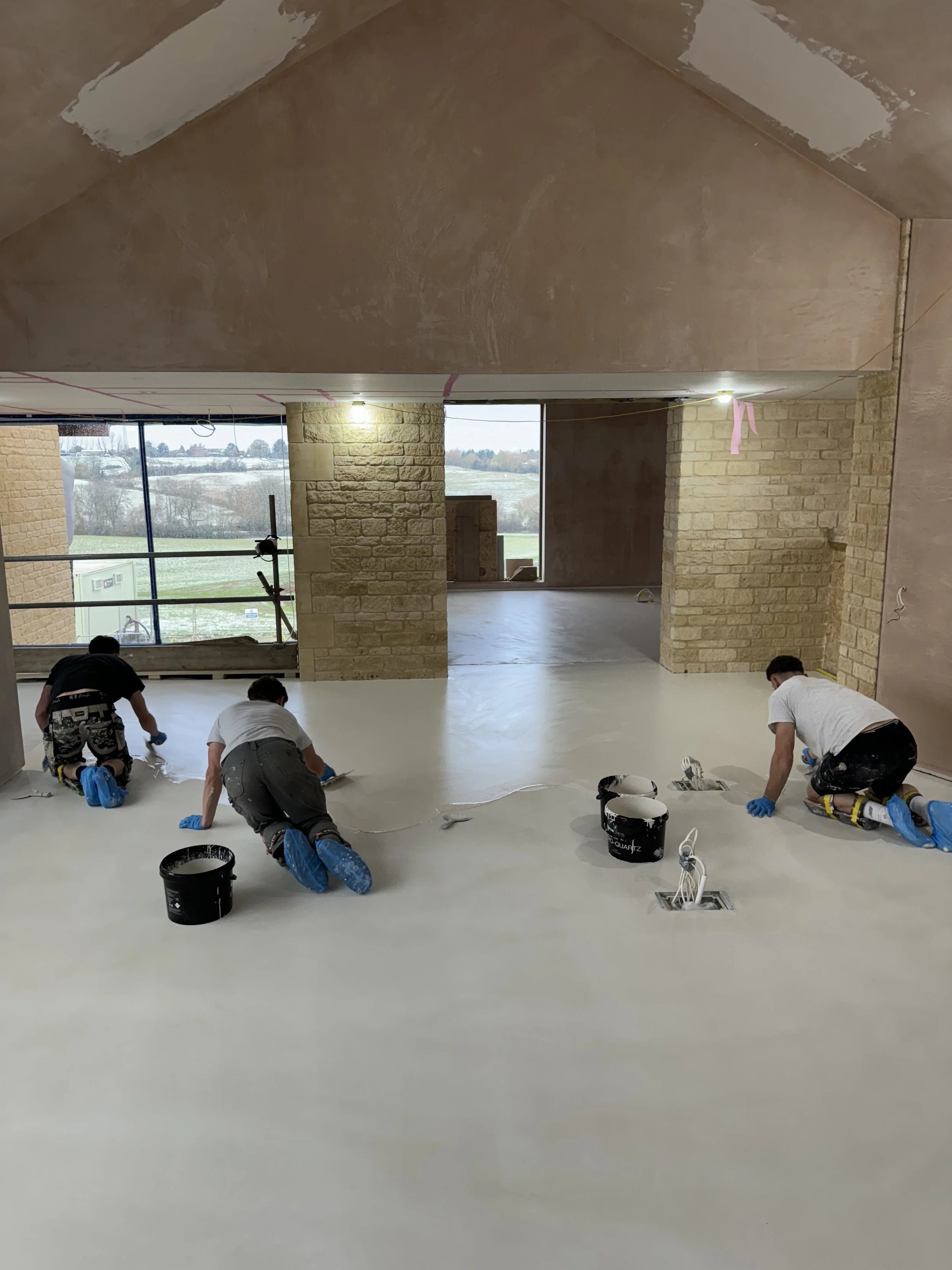 Instaladores aplican un acabado continuo en el piso de un interior / Installers apply a seamless floor finish inside a building.
