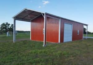 A red metal barn with a covered side bay in a grassy field. / Granero metálico rojo con un espacio lateral techado en un terreno con césped.