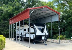 A recreational vehicle parked under an open-sided metal carport. / Vehículo recreativo estacionado bajo una cochera metálica abierta.