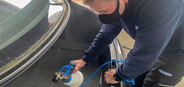 A technician checking a car window for a water leak. / Un técnico revisa una ventanilla para detectar una filtración de agua.