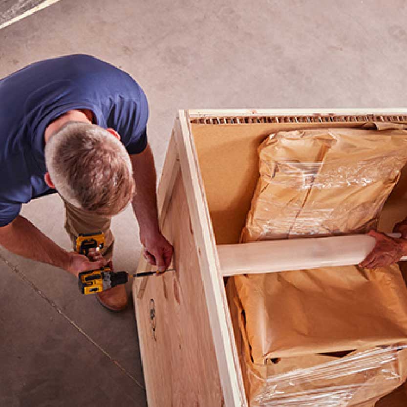 Especialista construye una caja de madera a medida para proteger un objeto durante el envío. / A specialist builds a custom wooden crate to protect an item in transit.