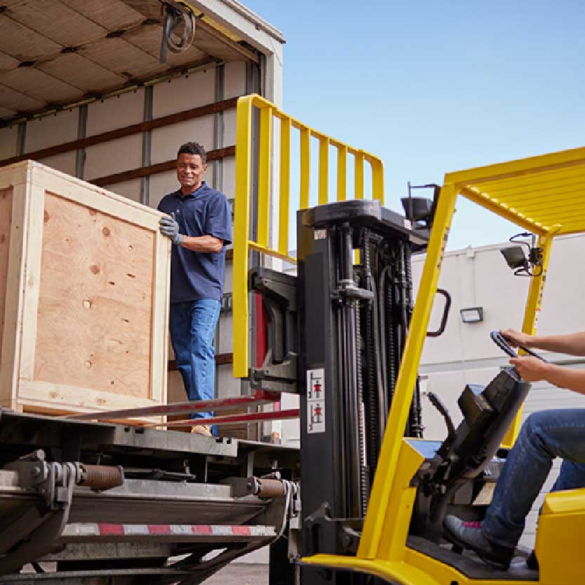 Equipo de embalaje carga una caja de madera en un vehículo de transporte. / A packing crew loads a wooden crate onto a transport vehicle.