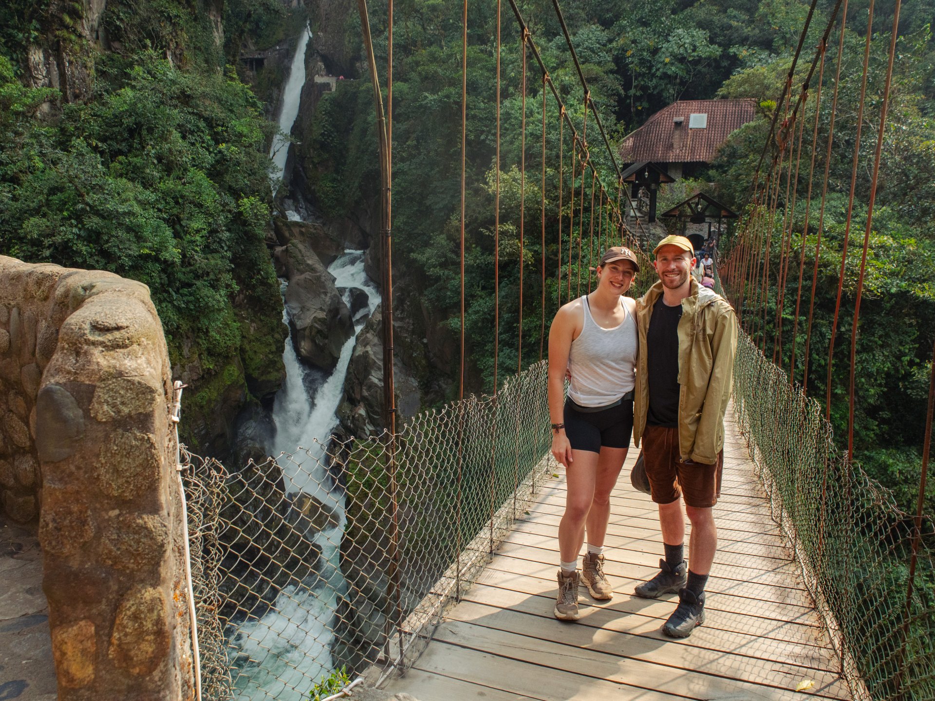 Viajeros cruzan un puente colgante junto a una cascada en Baños