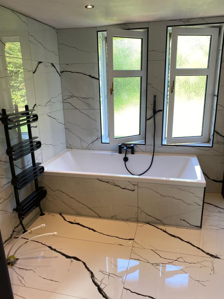 Bathroom with a bathtub and marble-patterned tiling shown by OBW Bathrooms