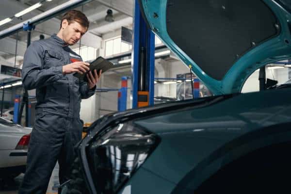 Technician consulting a tablet while diagnosing a car in a workshop