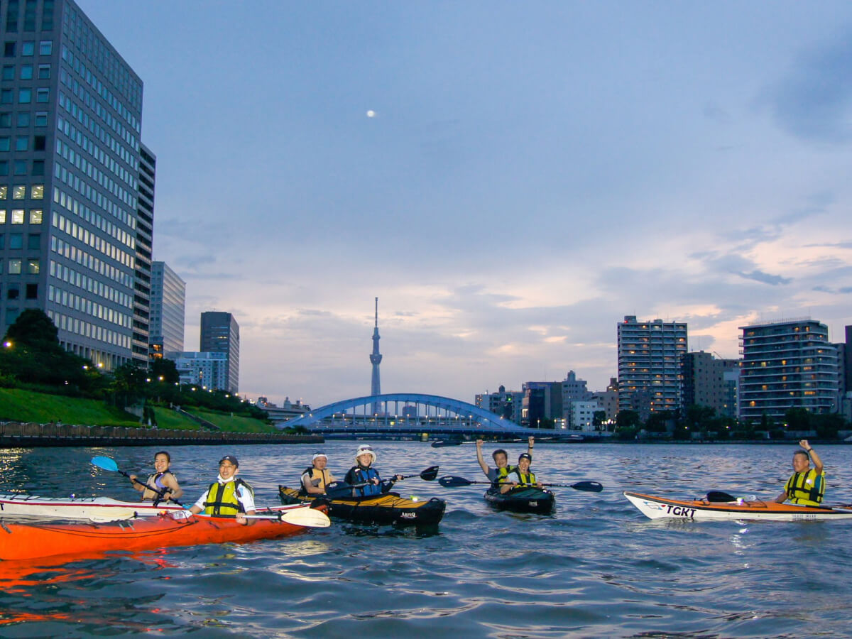Kayaks avanzan por un canal urbano de Tokio al atardecer