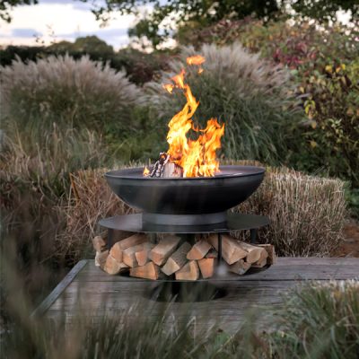 Outdoor fire bowl burning above a stack of logs